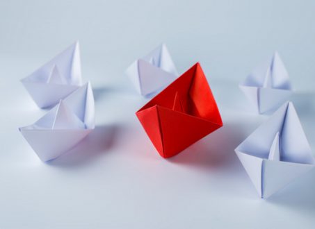 Barco de papel rojo liderando a barcos de papel blancos